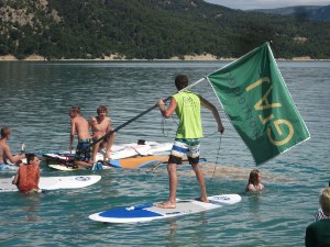 Kinderbetreuung auf dem Lac de Ste. Croix. Jugendliche auf Surfbrettern und Teamer mit Fahne.